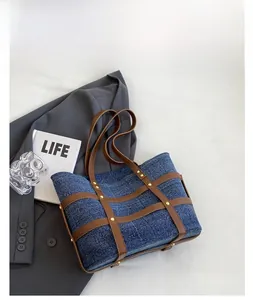 Detail of dark blue denim tote bag with brown straps, rivets and chic retro styling