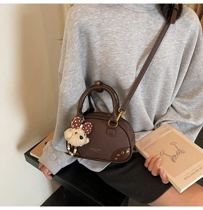 Detail of dark brown leather Boston bag with rivet trim and cute puppy plush charm