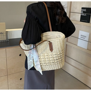 Detailed close-up of layered straw tote bag featuring leather handles and floral silk scarf