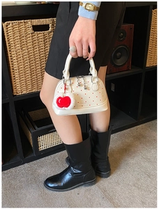 Detail of white leather mini bag with red dots and cute apple charm shown by a model