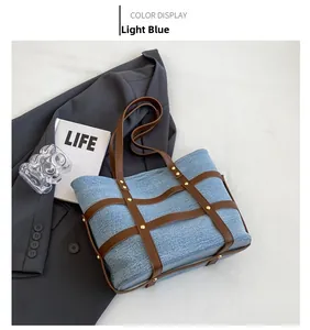 Detail of light blue denim tote bag featuring brown leather straps and gold rivets