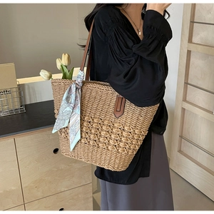 Detail of hand-woven straw tote bag with brown leather straps and floral scarf decor