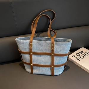 Detail of blue denim tote bag with brown leather trim and golden metal rivet accents