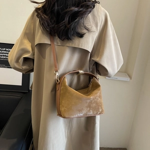 Woman in khaki coat carrying a mustard yellow suede crossbody bag in a modern setting