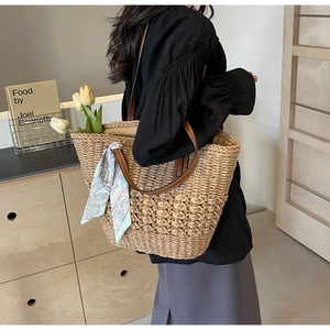 Detail of hand-woven straw tote bag with brown leather handles and decorative silk scarf