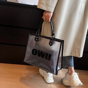 Detail of clear frosted PVC tote bag with black leather handles and OWU lettering