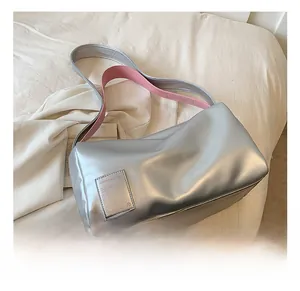 Detail of silver metallic pillow bag with contrasting bright pink strap and logo patch