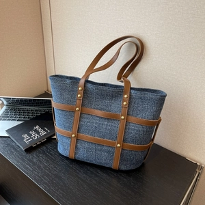 Detail of blue denim tote bag with brown leather straps and gold metal rivets on a desk
