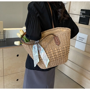 Close-up of woven straw tote bag with brown leather straps and vintage print scarf decor