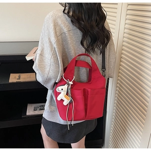 Dettaglio macro della borsa tote in tela rossa con tasche esterne e ciondolo peluche