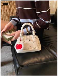 Detail of white shell handbag with red polka dots and apple pompom charm on a sofa