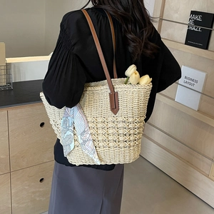 Minimalist straw tote bag with brown leather handles and a colorful floral silk scarf