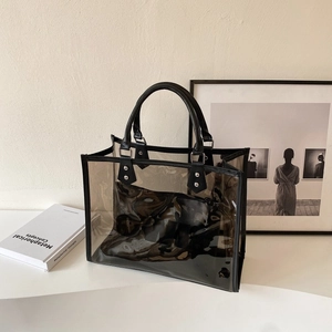 Modern transparent PVC tote bag with black inner pouch and metallic rivets in a studio setting