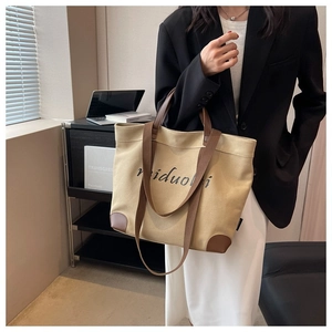 Detail of khaki canvas tote bag featuring brown leather reinforcement and dark shoulder straps