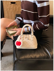 Detailed view of white mini Boston bag with red polka dots and apple charm accessory