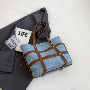 Large denim tote bag with leather trim and gold studs on a neutral lifestyle background