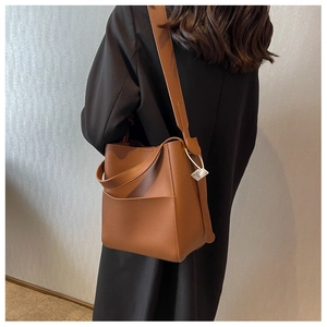 Sac seau en cuir grainé marron avec bandoulière large porté par un mannequin en extérieur
