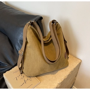 Detail of mustard yellow canvas hobo bag with round leather logo on a stone base
