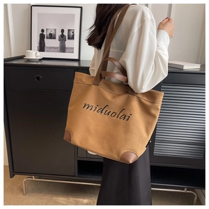 Brown canvas tote bag with leather trim and miduolai text shown on model's shoulder