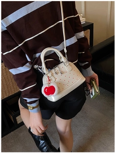 Detailed view of cream polka dot shell bag with apple charm worn as a crossbody bag