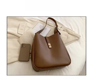 Close-up of caramel brown leather bucket bag with gold clasp and phone for size reference