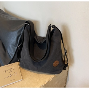 Detail of black canvas hobo bag with brown leather logo patch and adjustable wide strap
