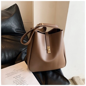 Detail view of a dark brown bucket bag with a gold metal buckle on a black leather seat