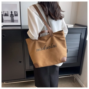 Lifestyle shot of a brown canvas tote bag with leather corner accents and brand lettering