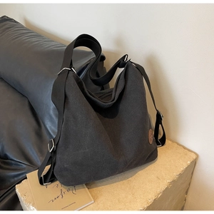 Close-up of black canvas tote bag with adjustable strap and round brown leather logo patch