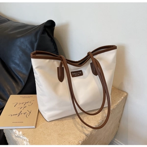 Detail der großen beigen Oxford-Tasche mit braunem Lederbesatz und modischem Aufnäher