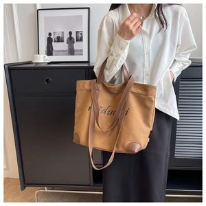 Close-up of brown canvas tote bag with leather straps and printed brand logo design