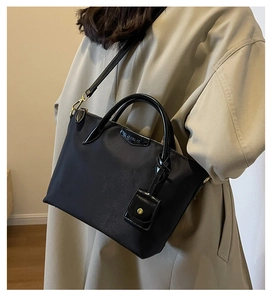 Detailed view of black nylon tote bag with leather handles on a trench coat model