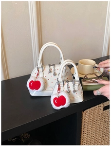 Detailed macro view of white shell bag with red polka dots and apple-shaped plush charm