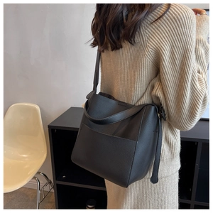 Détail du sac seau en cuir noir grainé avec bandoulière large sur une robe