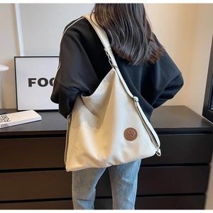 Detailed view of large canvas tote bag with brown leather logo patch and metal rings