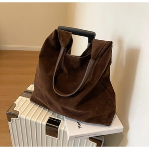 Deep brown matte suede tote bag placed on white luggage for a casual travel scene view