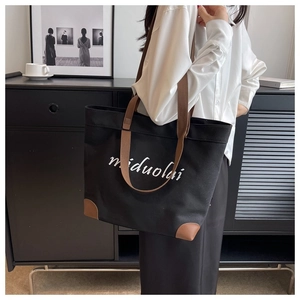 Detail of black canvas tote bag showing brown reinforced corners and woven shoulder straps