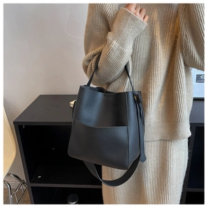 Sac seau chic en cuir noir avec large bandoulière porté par un mannequin en beige