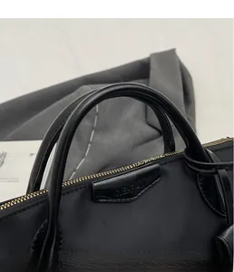 Close-up of black nylon tote bag featuring gold zippers and premium leather handles