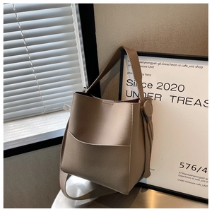 Détail du sac seau beige montrant le cuir grainé litchi et l'attache latérale en métal