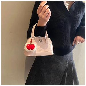 Detailed side view of pink polka dot shell bag with a cute plush cherry charm accessory