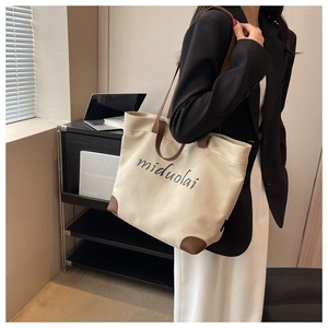 Detail of canvas tote bag with brown leather reinforcement and artistic printed text