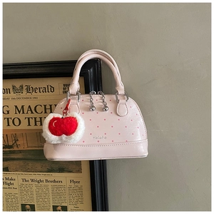 Detailed close-up of pink polka dot shell bag with plush apple charm and metallic zipper