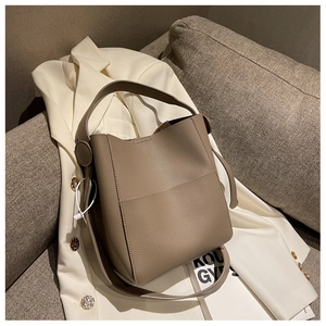 Détail d'un sac seau en cuir grainé gris éléphant avec bandoulière sur blazer blanc
