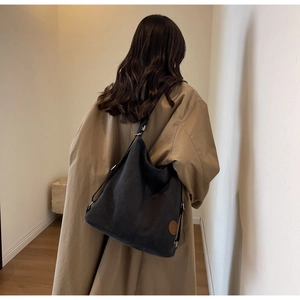 Rear view of model wearing a large black canvas tote bag against a minimalist indoor background