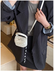Detail of a white mini bag with lace trim, metallic bow, and pearl studs on model