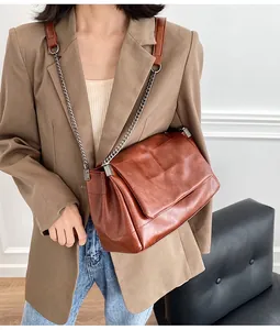 Détail d'un sac bandoulière matelassé marron avec chaîne sur un mannequin portant un costume