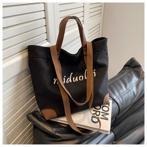 Detail of black canvas tote bag with leather straps on black leather sofa