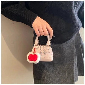 Pink polka dot mini shell bag with red apple plush charm held by a model in black