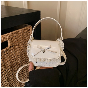 Detail view of white lace mini handbag with heart pendant and bow on glossy leather